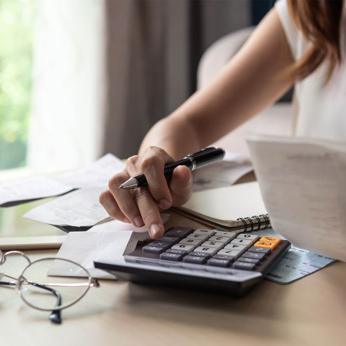 Someone typing into a calculator on a desk with papers on it