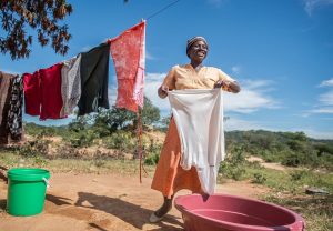 A woman hanging laundry from a pink bucket while smiling in the sun